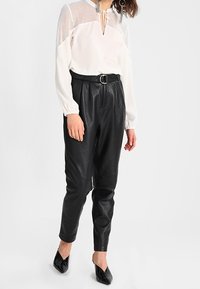 Vit blus med mesh-axlar och detalj med knytning, kombinerad med svarta högmidjade läderbyxor och svarta spetsiga ballerinaskor.