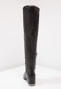 Botte en cuir noir montante avec une texture lisse et une fermeture éclair sur le côté. Talon épais et semelle blanche apportent du contraste. Design simple.