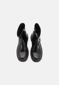 Botines de charol negro con un acabado brillante, cremallera lateral y una correa con hebilla en la parte frontal; suela de goma texturizada.