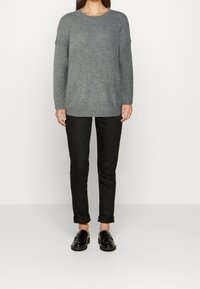 Szary dziergany sweter o prążkowanej fakturze, z okrągłym dekoltem i opuszczonymi szwami na ramionach. Połączony z czarnymi, podwiniętymi spodniami i czarnymi mokasynami.