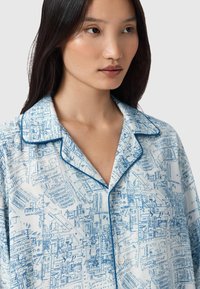 Sininen ja valkoinen kuviollinen pyjamapaita, jossa on karttakuva, kontrastivärinen sininen piping kauluksessa ja nappikiinnitys edessä.