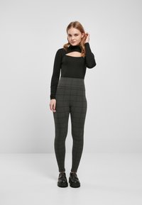 Black long-sleeve bodysuit with cutout detail paired with high-waisted, gray plaid leggings. Model wears chunky black loafers.