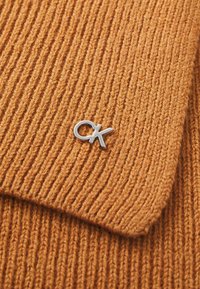 Pulover tricotat dintr-un material texturat de culoare portocalie, cu dungi verticale și un accent cu logo-ul argintiu "CK" la guler.