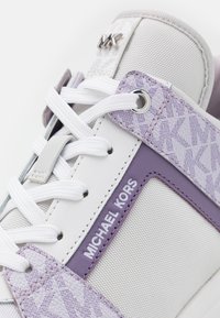 White and lavender sneaker with fabric and leather panels, textured pattern, metallic accents, and flat laces; features brand name on side.