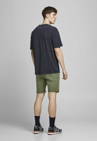 Camiseta de algodón azul marino con cuello redondo, combinada con pantalones cortos de color verde oliva. Los pantalones cortos están doblados en el dobladillo. Unos zapatos deportivos en negro y gris complementan el look.