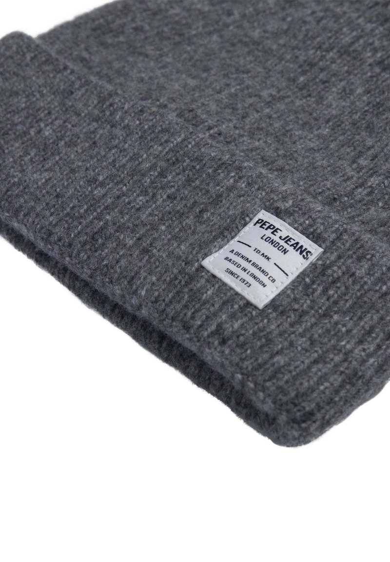 Beanie grigio lavorato a maglia con una texture morbida e risvolto. Presenta un'etichetta bianca con testo nero; nome del marchio e origine visibili.