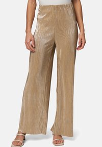 Pantalons larges à plis dorés avec une texture brillante, dotés d'une taille élastique et d'une coupe ample. Associés à des sandales de couleur claire.