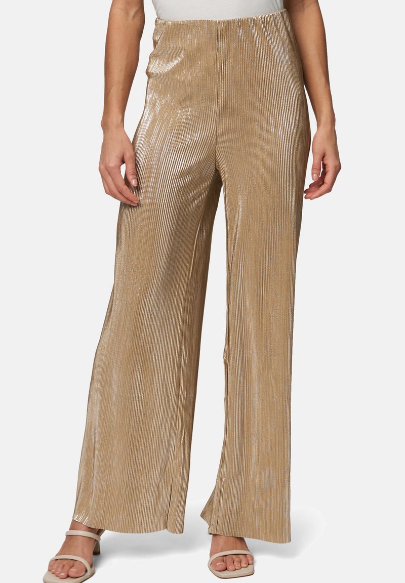 Pantalons larges à plis dorés avec une texture brillante, dotés d'une taille élastique et d'une coupe ample. Associés à des sandales de couleur claire.