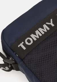Granatowa torba na ramię z teksturowaną siateczkową sekcją i czarnym paskiem. Posiada białe logo "TOMMY" na górnej części, podkreślające jej design.