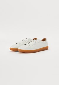 Baskets en cuir blanc avec détails perforés, lacets plats et semelle en caoutchouc beige. Bout rond et design bas.