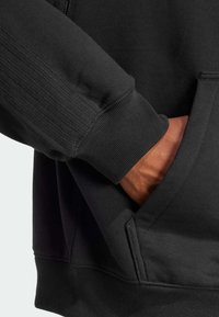 Melna sporta krekls ar ribotām aprocēm, teksturētu šuvju detaļām un priekšpusi kabatu. Mīksta materiāla, br�īvs griezums.