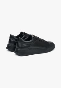 Czarne skórzane sneakersy o gładkiej fakturze, niskim profilu, okrągłym nosku, grubej podeszwie i subtelnych detalach w postaci przeszyć.
