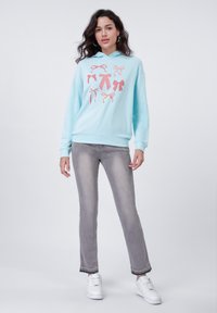 Felpa azzurra chiara con stampe di nastri rosa, abbinata a jeans grigi sbiaditi e sneakers bianche. Presenta un cappuccio e polsini a coste.