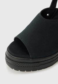 Sandale en toile noire avec un design à bout ouvert, semelle noire texturée avec un motif en diamant et un dessus lisse avec des bords cousus.