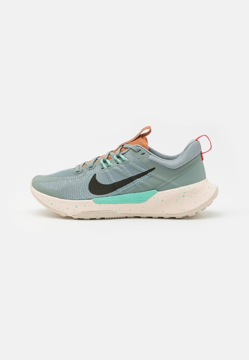 Chaussure de course Nike en gris clair et turquoise. Présente un logo swoosh noir, des accents orange, et une semelle éclatée pour plus de texture.