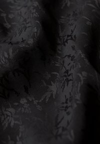 Tejido negro texturizado que presenta un sutil patrón floral, con un suave brillo y una superficie lisa. Tejido de alta calidad con detalles intrincados.