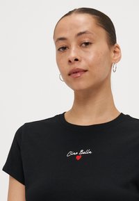 Zwarte katoenen t-shirt met een ronde hals, voorzien van rode geborduurde tekst "Ciao Bella" en een klein hartenmotief op de borst. Soepele textuur.