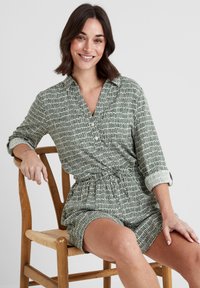Green patterned shirt dress with a collar, rolled sleeves, drawstring waist, and a short cut, made from a lightweight, textured fabric.