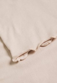 Tessuto di cotone beige con una morbida trama, caratterizzato da bordi arricciati e cuciture visibili. Leggero e morbido al tatto.