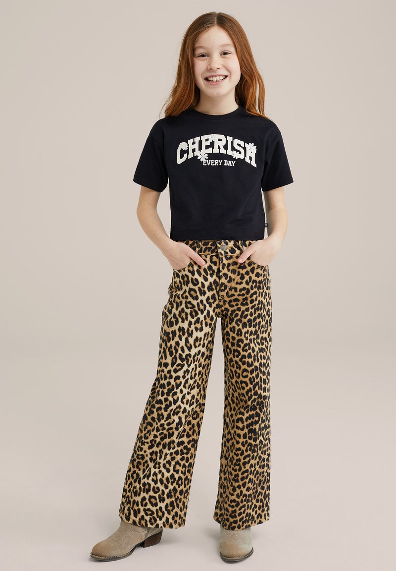 Svart kortärmad t-shirt med texten "CHERISH EVERY DAY", kombinerad med tan breda byxor med svart leopardmönster. Beige ankelskor.