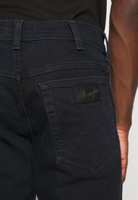 Jeans de mezclilla azul oscuro, con una etiqueta de cuero de la marca y detalles de costura sutiles en los bolsillos traseros.