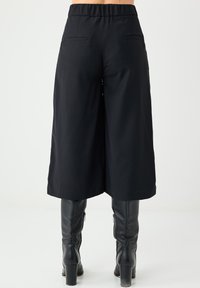Czarne szerokie kuloty z elastycznym pasem, dwiema tylnymi kieszeniami oraz gładką fakturą materiału. W połączeniu z czarnymi botkami do kolan.