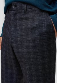Navy geblokte broeken van een gestructureerde stof, met een voorzak en een knoopsluiting, voorzien van een subtiel geruit ontwerp.