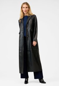 Svart läderlångjacka med spetsig krage, knapstängning och framfickor. Har en jämn textur och en skräddarsydd passform.