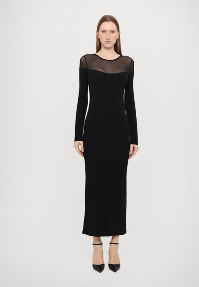 Langes schwarzes Kleid mit einer taillierten Silhouette. Durchsichtiger Mesh-Ausschnitt und -Ärmel. Glattes, leichtes Material. Getragen mit schwarzen spitzen Absätzen.