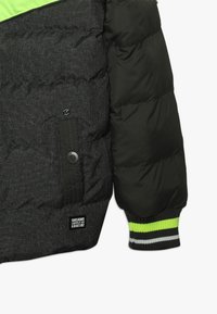 Puffig svart jacka med en strukturerad grå tyg och neongröna detaljer. Har ribbade ärmslut med randig dekoration och en ficka med tryckknapp.