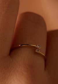 Bague en or avec un anneau lisse, présentant deux petites pierres rondes transparentes positionnées sur le dessus dans un design minimaliste.