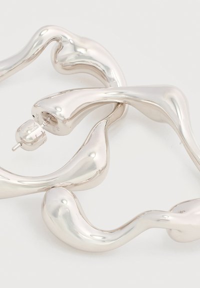 Ασημί, αφηρημένα σπειροειδή σκουλαρίκια κρίκοι με λεία, γυαλιστερή επιφάνεια και πίσω κούμπωμα σε λευκό φόντο.
