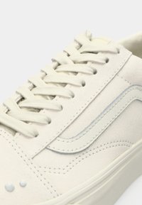 Ανοιχτό μπεζ σουέτ αθλητικά παπούτσια με επίπεδα κορδόνια, χαρακτηριστική πλευρική ρίγα σε ανοιχτό γκρι χρώμα, και μικρές διακοσμητικές λεπτομέρειες κοντά στο δάχτυλο.