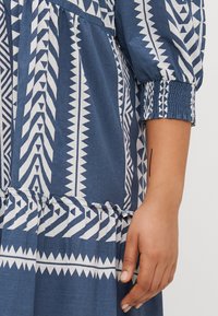 Abito blu a motivi con disegni geometrici bianchi, maniche arricciate con accenti elasticizzati e orlo a strati con dettagli arruffati.
