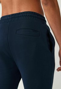 Pantalones de chándal azul marino con cintura elástica, bolsillos laterales y un bolsillo trasero, con una textura suave y un diseño informal.