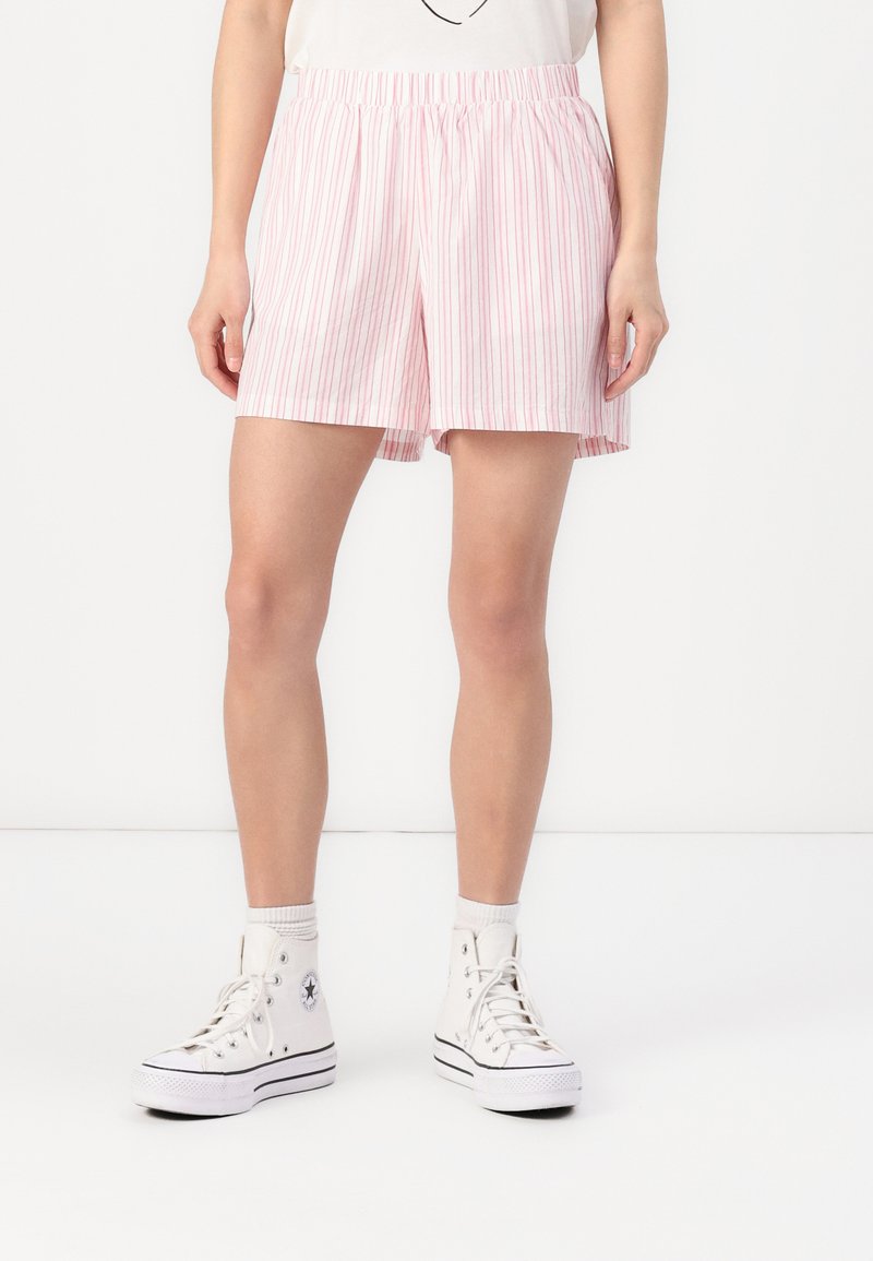 Lyse rosa stripet shorts med elastisk midje, avslappet passform og sidelommer, paret med hvite høyhælte sneakers.