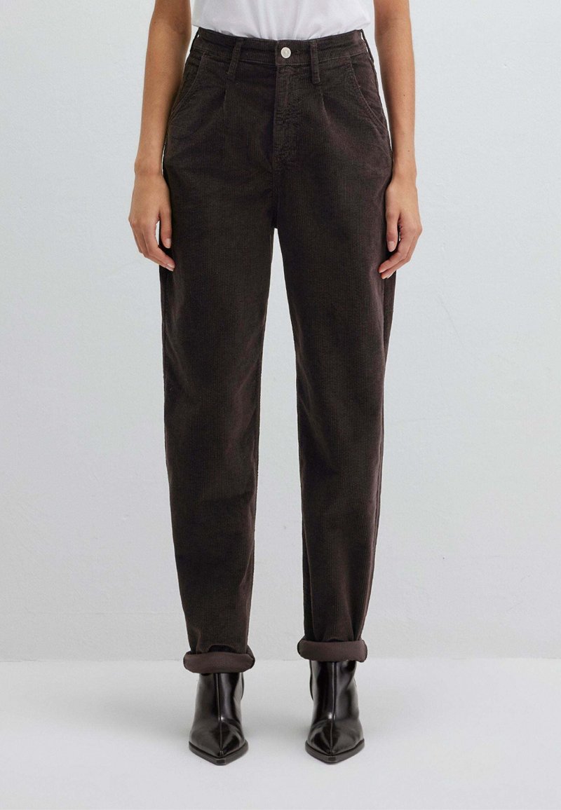 Pantaloni di velluto a coste marroni con vestibilità rilassata, dotati di tasche laterali e risvolti arrotolati, abbinati a stivaletti neri con punta appuntita.