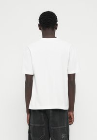 Λευκό βαμβακερό μπλουζάκι με κλασική εφαρμογή, κοντά μανίκια και ίσια βάση. Χωρίς ορατά σχέδια ή γραφικά. Δείχνεται από πίσω.