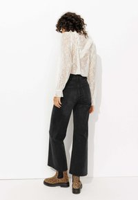 Blouse blanche à manches longues en dentelle avec un col à volants, associée à un jean noir à taille haute et jambes larges, et des bottines à imprimé léopard.