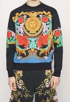 Sweat-shirt noir avec motifs floraux baroques ornés en or, rouge, turquoise et violet, avec un emblème central représentant le soleil et le texte "Versace Jeans Couture".