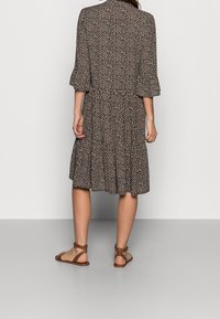 Svart och crème mönstrad klänning med ett lager på lager-skirt, trekvartslånga ärmar och en rundad krage. Bärs med bruna platta sandaler.