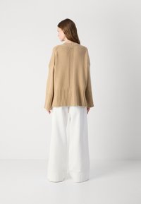 Beige oversized trui met ribbeltextuur en zoom, met een lage achterkant en verlaagde schouders, gecombineerd met witte wijde broekspijpen.