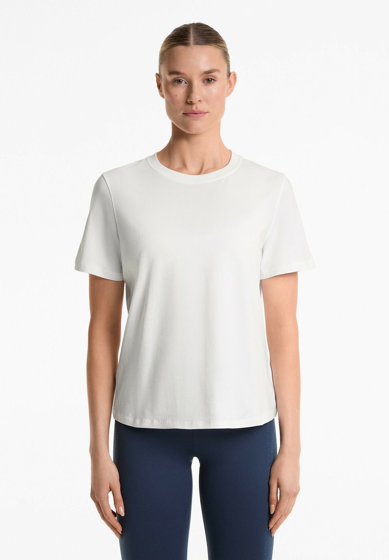 T-shirt bianco a maniche corte con scollatura rotonda, texture morbida, vestibilità rilassata e orlo dritto. Abbinato a leggings blu navy.
