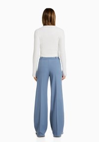 Light blue wide-leg trousers with a smooth texture, front pleats, and a high waist. Paired with a fitted white long-sleeve top.