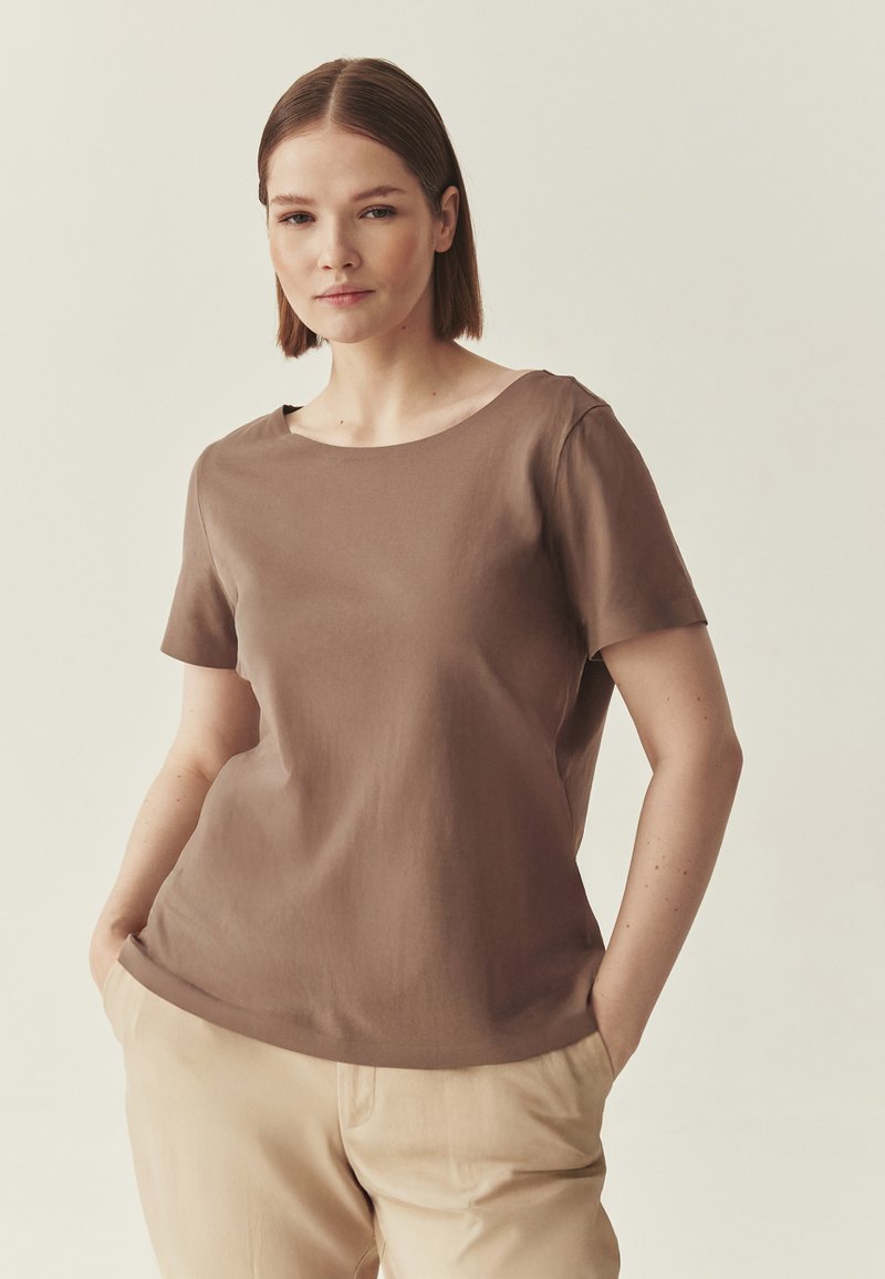 T-shirt marron à manches courtes avec un col rond, fabriqué en tissu lisse. Associé à un pantalon beige clair, doté d'une coupe décontractée.