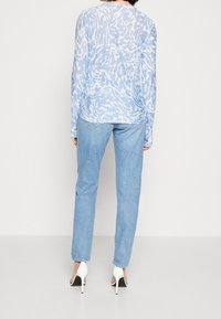 Helles blaues gemustertes Langarmoberteil mit lockerer Passform, kombiniert mit hellblauen geraden Jeans und weißen High-Heel-Schuhen.