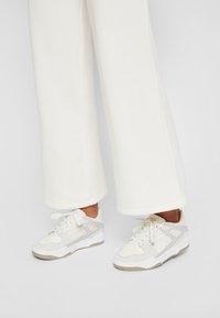 Baskets blanches avec accents gris, présentant un mélange de matériaux lisses et texturés, des lacets ronds et un design profilé bas.