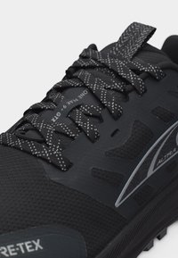 Κοντινό πλάνο μαύρου αθλητικού παπουτσιού με ανακλαστικά κορδόνια με σχέδιο, αναπνέον δίχτυ και λογότυπο της μάρκας στο πλευρό, σε ανθεκτική σόλα.