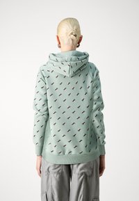 Sudadera con capucha verde menta, con un patrón repetitivo de pequeños triángulos rojos y verdes. Tejido suave con un ajuste holgado.