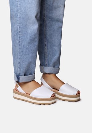 White platform sandals with an open toe and back strap. Features a smooth synthetic upper, layered beige sole, and textured rubber bottom.